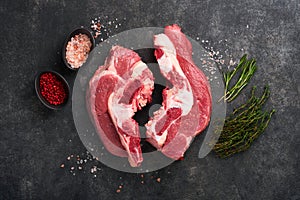 Raw beef meat. Rough piece of meat on bone for roast or soup with salt, pepper, thyme and rosemary on a black concrete background