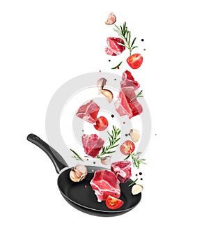 Raw beef meat steaks with different ingredients are falling into a frying pan isolated on white background