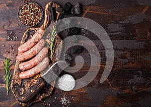 Raw beef and pork sausage on old chopping board with vintage knife on dark wooden background.Salt and pepper with rosemary.Space