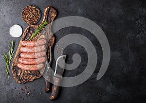 Raw beef and pork sausage on old chopping board with vintage knife and fork on black background.Salt and pepper with rosemary.