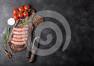 Raw beef and pork sausage on old chopping board with vintage knife and fork on black background.Salt and pepper with rosemary and