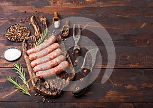 Raw beef and pork sausage on old chopping board with vintage knife and fork on dark wooden background.Salt and pepper with