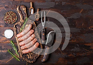Raw beef and pork sausage on old chopping board with vintage knife and fork on dark wooden background.Salt and pepper with