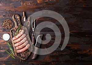 Raw beef and pork sausage on old chopping board with vintage knife and fork on dark wooden background.Salt and pepper with