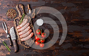 Raw beef and pork sausage on old chopping board with vintage knife and fork on dark wooden background.Salt and pepper with