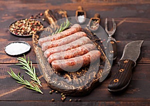 Raw beef and pork sausage on old chopping board with vintage knife and fork on dark wooden background.Salt and pepper with