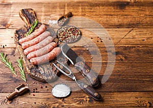 Raw beef and pork sausage on old chopping board with vintage knife and fork on wooden background.Salt and pepper with rosemary