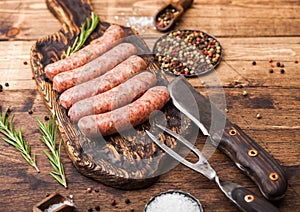 Raw beef and pork sausage on old chopping board with vintage knife and fork on wooden background.Salt and pepper with rosemary