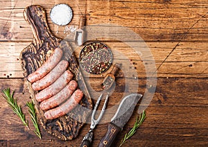 Raw beef and pork sausage on old chopping board with vintage knife and fork on wooden background.Salt and pepper with rosemary.