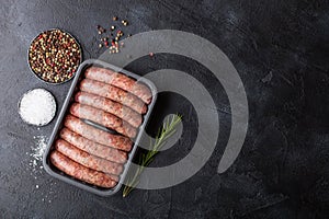 Raw beef and pork sausage in plastic tray with salt and pepper on black background. Space for text