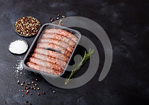 Raw beef and pork sausage in plastic tray with vintage fork on black background.Salt and pepper