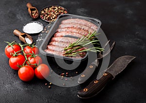 Raw beef and pork sausage in plastic tray with vintage knife and fork on black background.Salt and pepper with tomatoes and