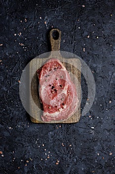 Raw beef rib eye steak on cutting board top view.