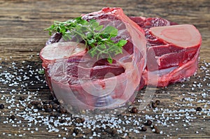 Raw beef shanks with herbs, black pepper and salt on old wooden background