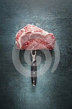 Raw beef steak with fork on dark concrete background