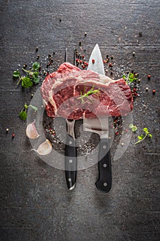 Raw beef steak with fork and knife salt pepper and herbs on dark concrete background