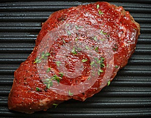 Raw beef steak with spices and thyme on the grill pan