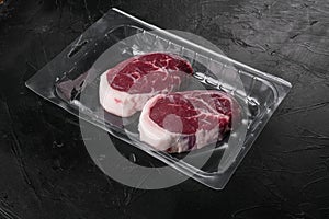 Raw beef steak in vacuum package, on black dark stone table background, with copy space for text