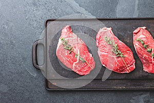 Raw beef steaks with herbs and spices on cast iron frying board, top view