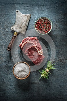 Raw beef steaks with meat cleaver and salt pepper on dark concrete background