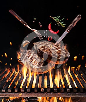 Raw beef steaks with vegetables and spices fly over the blazing grill barbecue fire