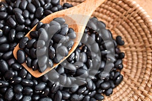 Raw black beans in basket and spoon on wood table