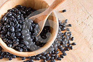 Raw black beans in wooden bowl and spoon on table