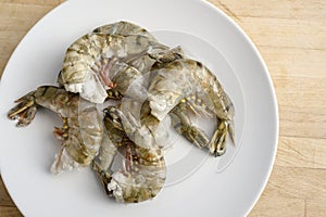 Raw black tiger prawn shrimps without head, cooking ingredients for a tasty dish on a white plate and a wooden kitchen worktop,