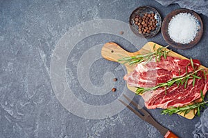 Raw blade steak of marbled beef on wooden board over dark background. Top view from above