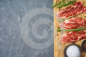 Raw blade steak of marbled beef on wooden board over dark background. Top view from above