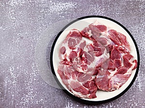 Raw blade steak from pork shoulder in a white plate on a dark background