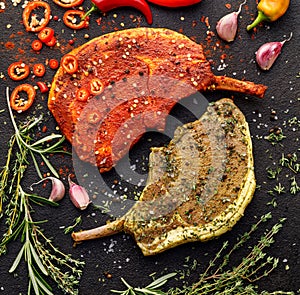 Raw bone-in pork chops, tomahawk steak marinated in aromatic marinades with fresh herbs and spices on a dark background