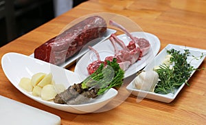 Raw boneless beef, bone rib-eye steak on a plate with onion, garlic and garnish ingredients on a kitchen table
