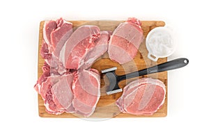 Raw boneless pork loin chops and meat tenderizer on a wooden cutting board