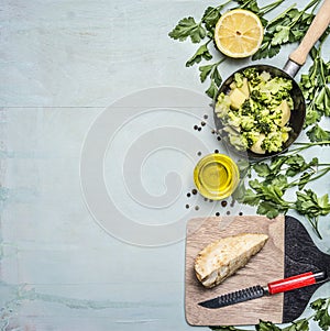 Raw broccoli in a pan with herbs, lemon, celery root on a cutting board with a knife border ,place text on wooden rustic backg