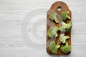 Raw broccoli on rustic cutting board on white wooden table, top view. Flat lay, overhead, from above.