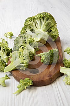 Raw broccoli on wooden cutting board on white wooden table