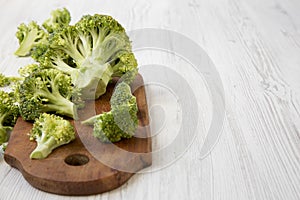 Raw broccoli on wooden cutting board on white wooden table, side view. Copy space