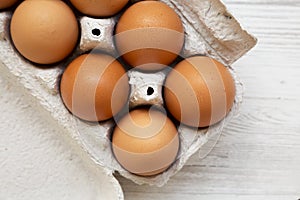 Raw Brown Eggs in a paper box on a white wooden background, top view. Flat lay, overhead, from above