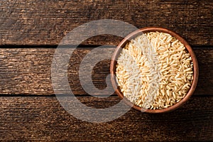 Raw brown rice in ceramic bowl on dark rustic wooden background