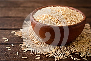 Raw brown rice in ceramic bowl on dark rustic wooden background