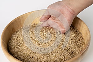 Woman`s hand is pouring raw brown rice packed in a plastic bag onto a wooden bowl