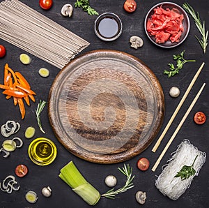 Raw buckwheat noodles with vegetables, ginger, chopsticks and ingredients, laid out around cutting board place for text,frame