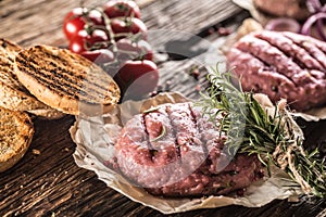 Raw burgers on wooden table with onion tomatoes herbs and spices