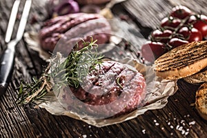 Raw burgers on wooden table with onion tomatoes herbs and spices