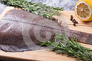 Raw butchered flounder on a cutting board with herbs and spices.