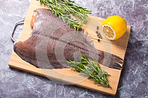 Raw butchered flounder on a cutting board with herbs and spices.