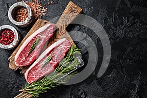 Raw cap rump beef meat steak or top sirloin on butcher board. Black background. Top view. Copy space