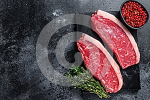 Raw cap rump steak or top sirloin beef meat steak on marble board. Black background. Top view. Copy space photo