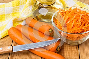 Raw carrot in bowl, bottle vegetable oil, knife and napkin